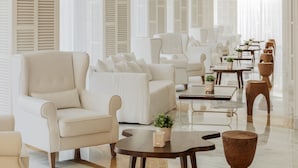 Un amplio y moderno salón con diversas opciones de asiento, incluyendo sofás y sillones, dispuestos alrededor de mesas y taburetes de madera.