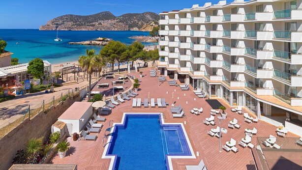 Un área de piscina en la azotea con vista al mar, sillas de descanso y un edificio con balcones.