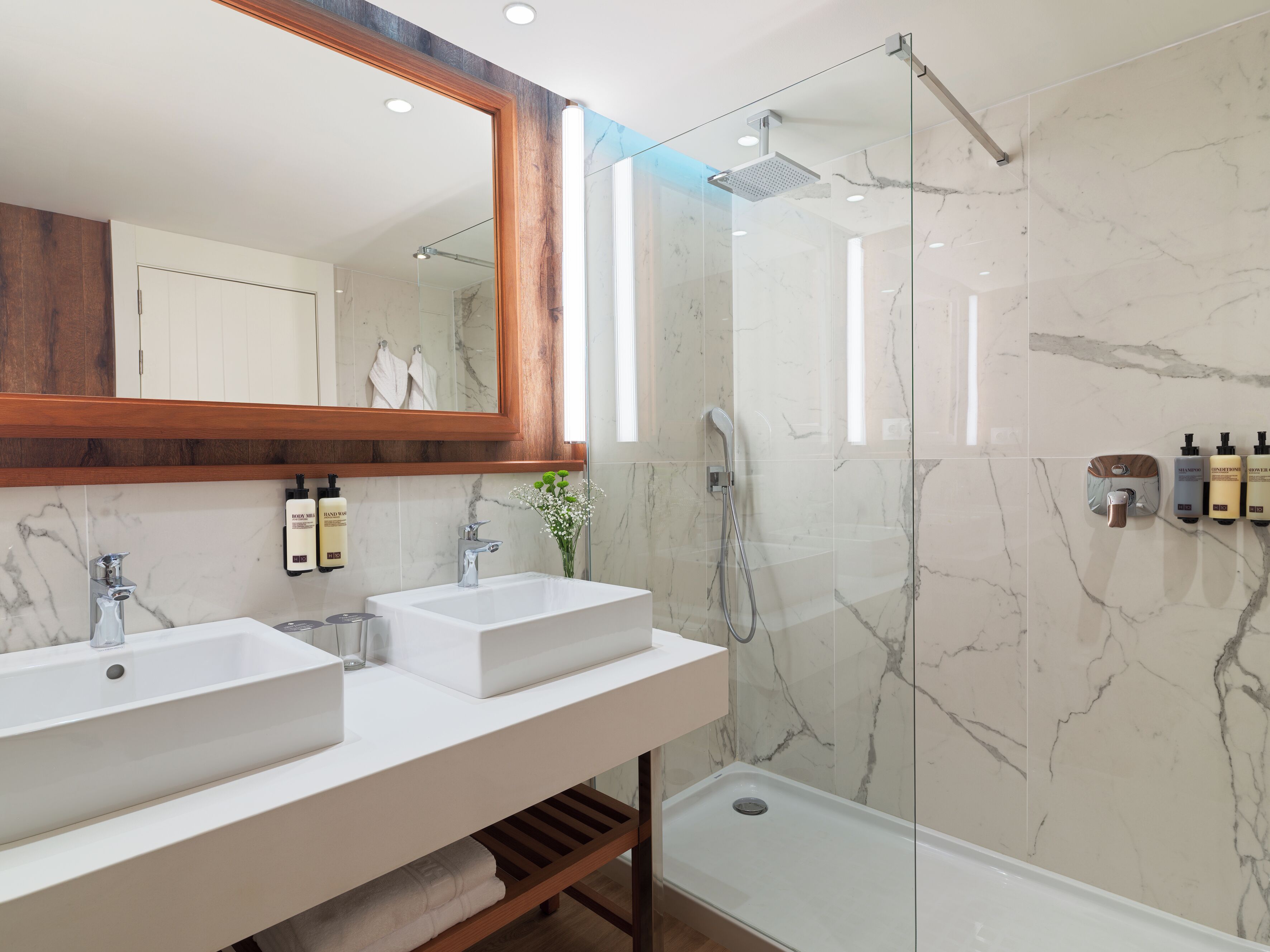 Un baño moderno con dos lavamanos, un espejo grande y cabina de ducha con mampara de vidrio.
