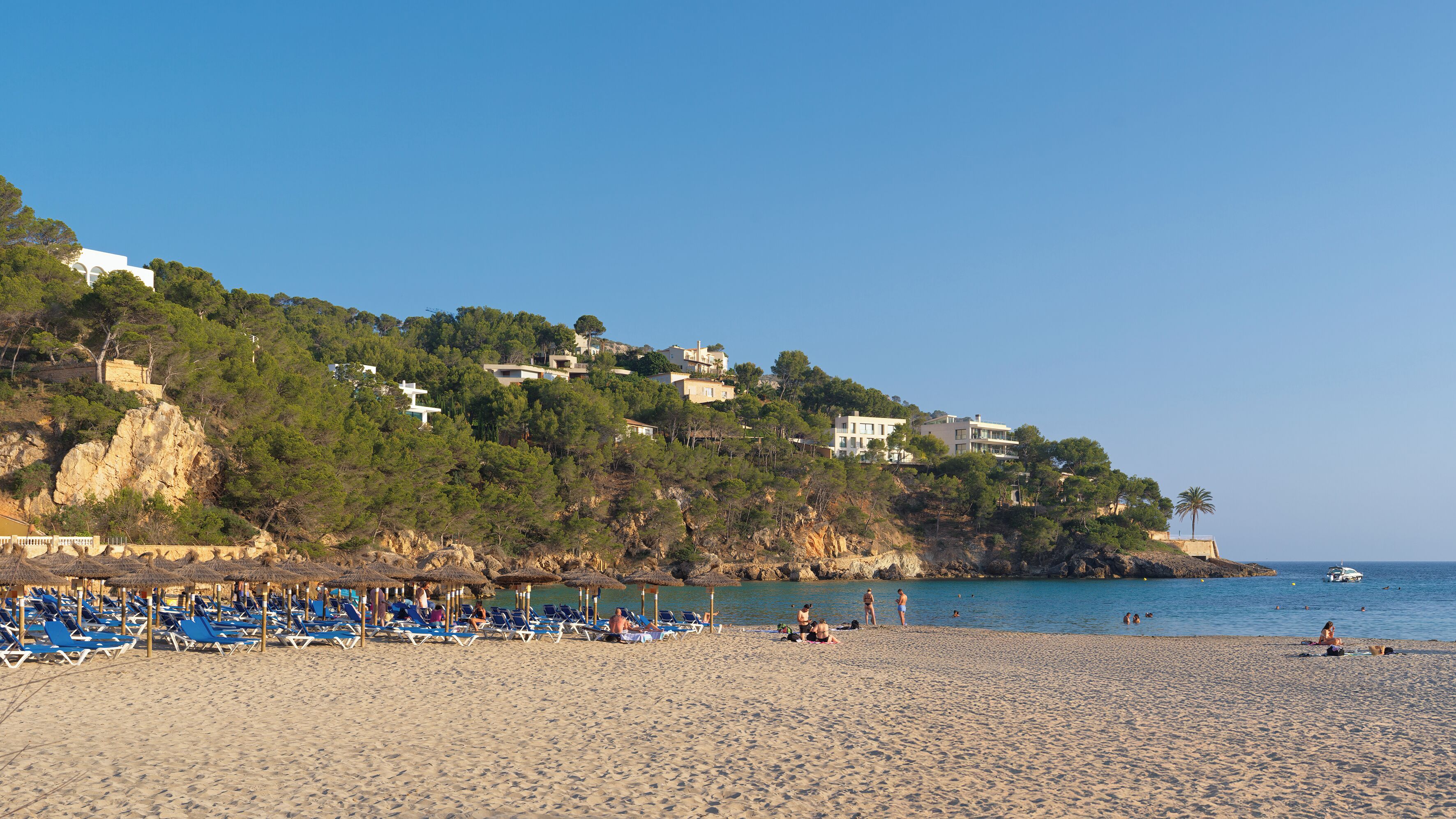 A beach with sun loungers and a rocky cliff with houses.