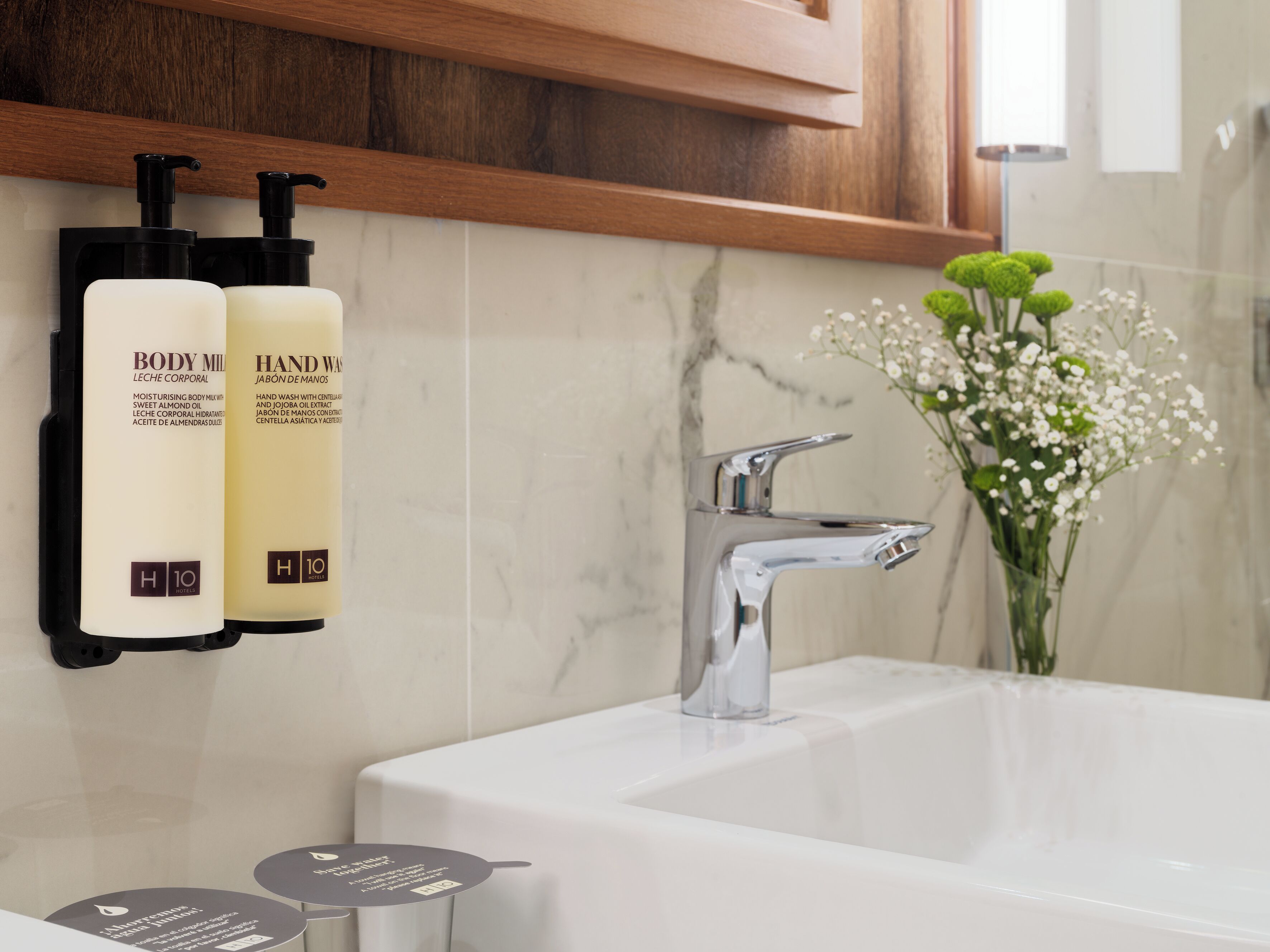 Un baño con pared de mármol, un grifo moderno y dos botellas de productos de cuidado corporal.