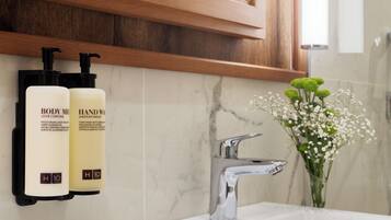 Un baño con pared de mármol, un grifo moderno y dos botellas de productos de cuidado corporal.