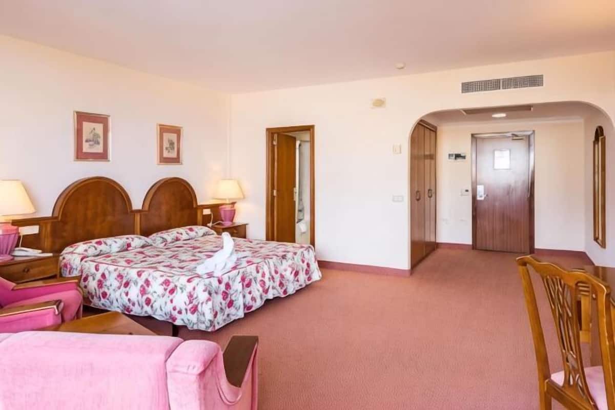 Habitación de hotel con cama doble, dos mesitas de noche, una silla, un escritorio y una puerta que da a otra habitación.