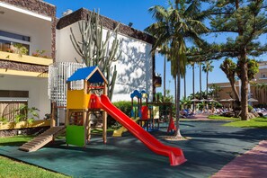 A playground with slides and climbing structures, surrounded by palm trees and a pool area with lounge chairs. - BLUESEA Puerto Resort (Puerto de la Cruz)