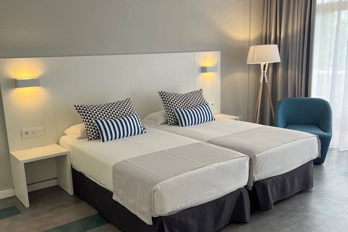 Habitación de hotel con dos camas, una mesita de noche, una lámpara y una silla.