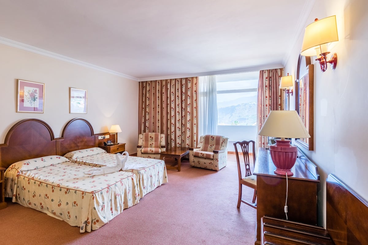 Habitación de hotel con dos camas, un escritorio, una silla y una ventana con cortinas.