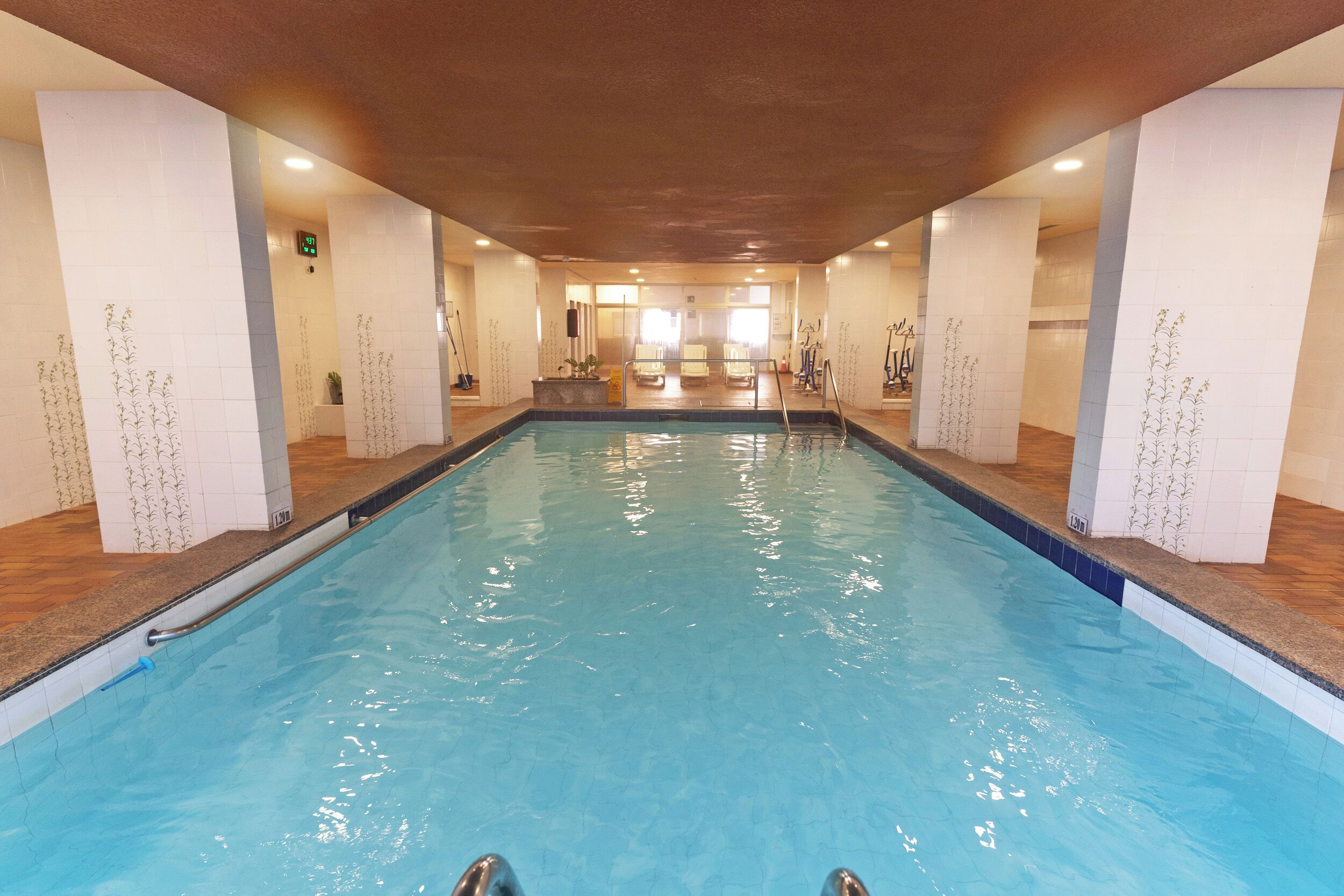 An indoor swimming pool with clear water, surrounded by tiled walls and wooden flooring.
