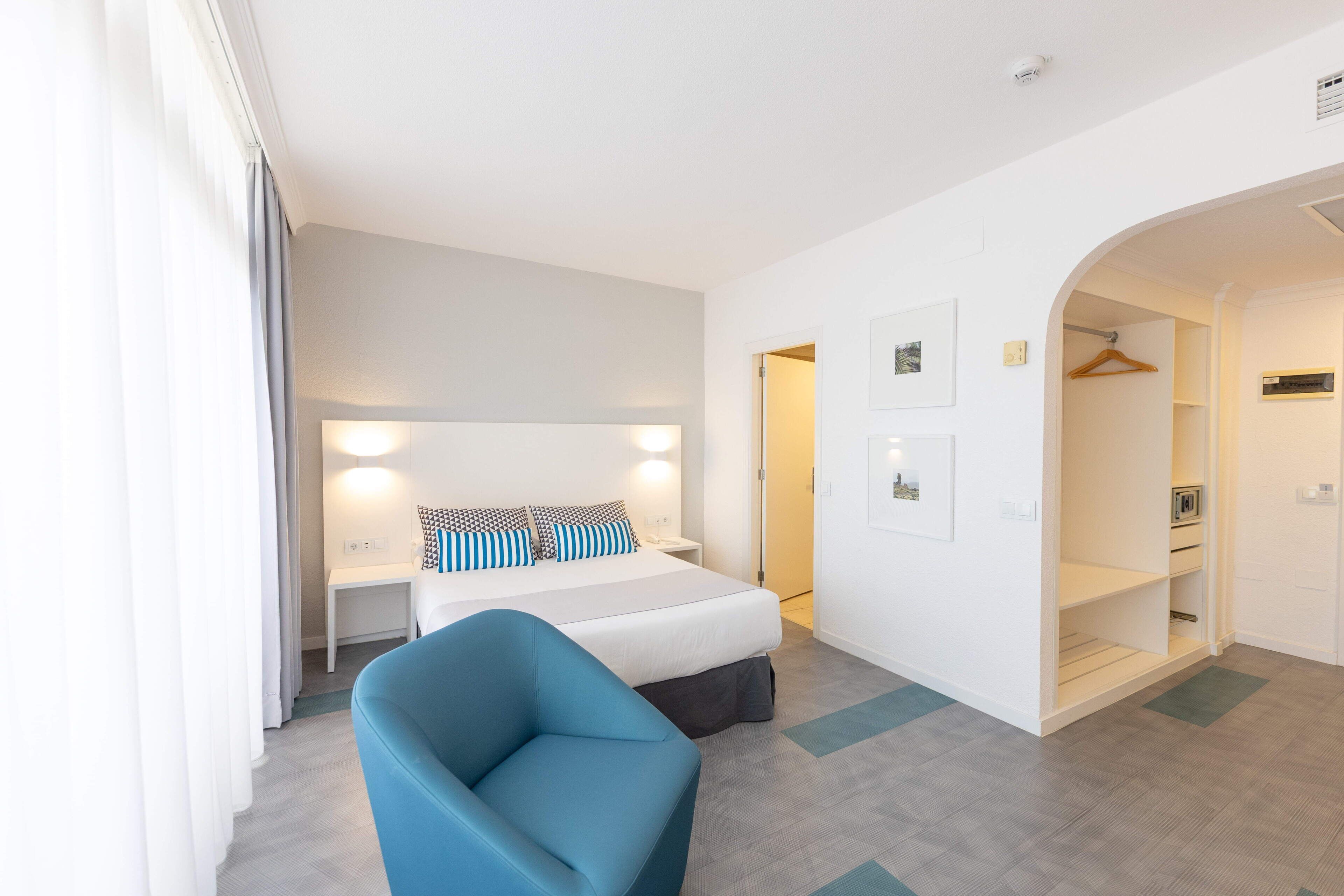 Habitación de hotel con cama, mesitas de noche, una silla, armario y puerta al baño.