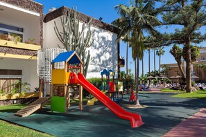Zona infantil con tobogán, estructuras de escalada y una casita.