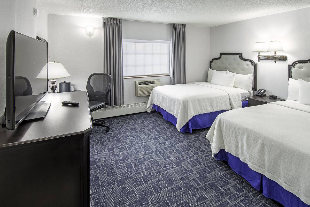 Habitación de hotel con dos camas, un escritorio con computadora, una silla y un ventanal con cortinas.