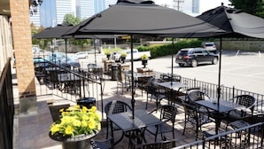 Un patio al aire libre con mesas y sillas, una zona de estar techada y un estacionamiento al fondo.