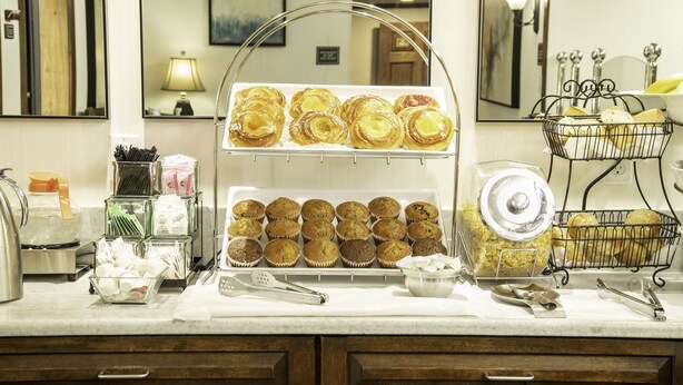 Un mostrador de buffet con diversas opciones de panadería, como muffins y pasteles, dispuestas en bandejas y cestas.