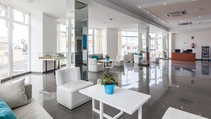 Um hall amplo com balcão de recepção, área de estar e grandes janelas com vista para o exterior.