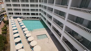Um hotel com vários andares, com uma piscina central rodeada por fileiras de espreguiçadeiras e guarda-sóis.