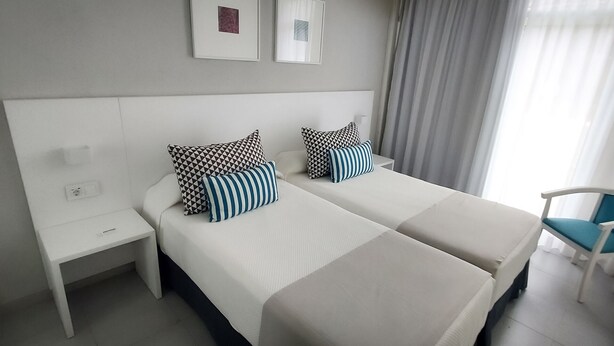 A hotel room with two beds, a nightstand, and a chair. - BLUESEA Lagos de Cesar (Santiago del Teide)