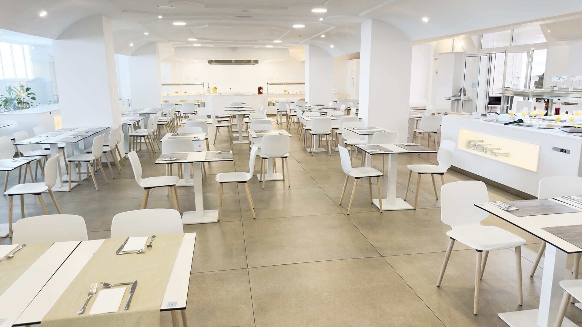 A modern dining area with white tables and chairs, a central counter with a display, and a bright, spacious layout.
