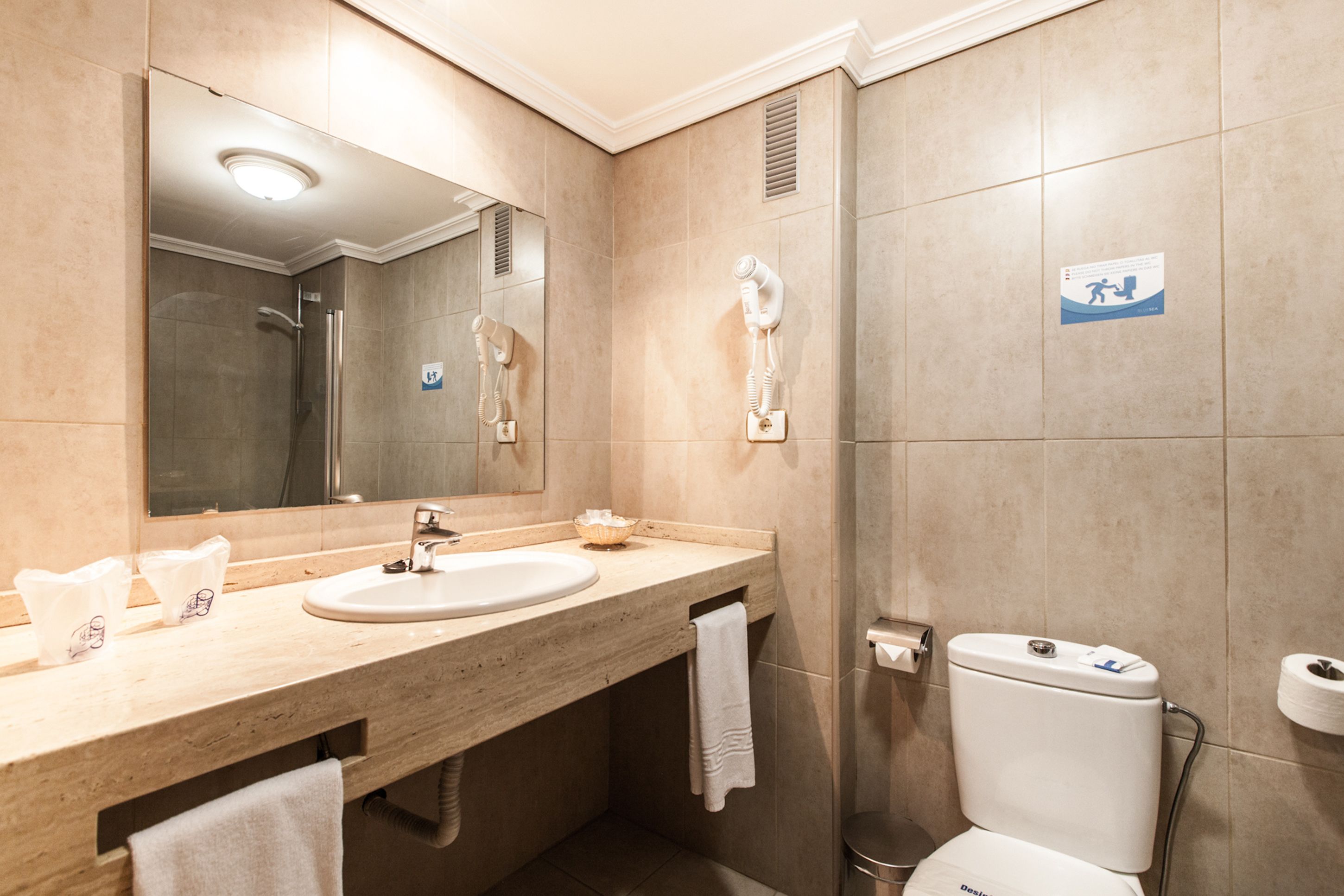 Et badeværelse med vask, spejl, håndklædetørrestativ og toilet.