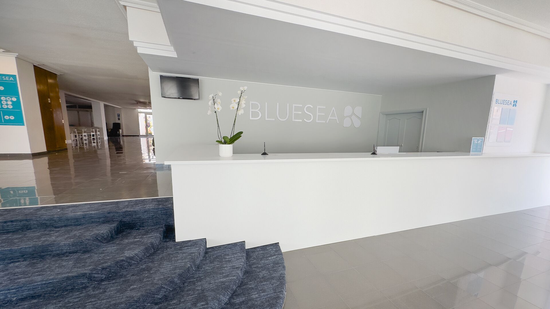 Zona de recepción con un cartel que dice "BLUESEA" y una escalera que lleva a un piso superior.