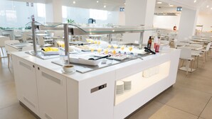 Uma área de buffet com uma vitrine de vidro, diversos alimentos e um relógio digital.