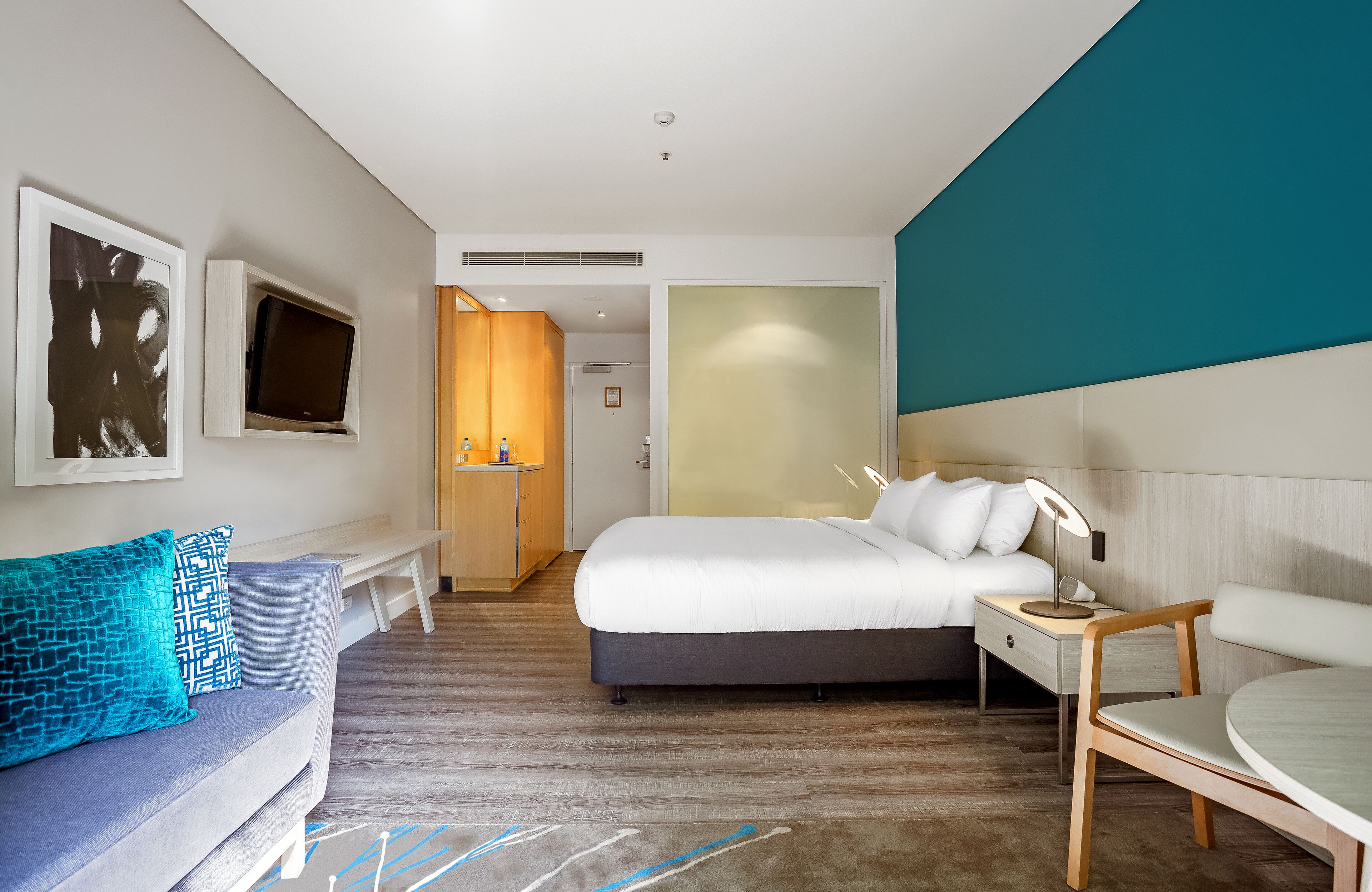 A modern hotel room with a bed, a desk, a chair, a sofa, and a television.