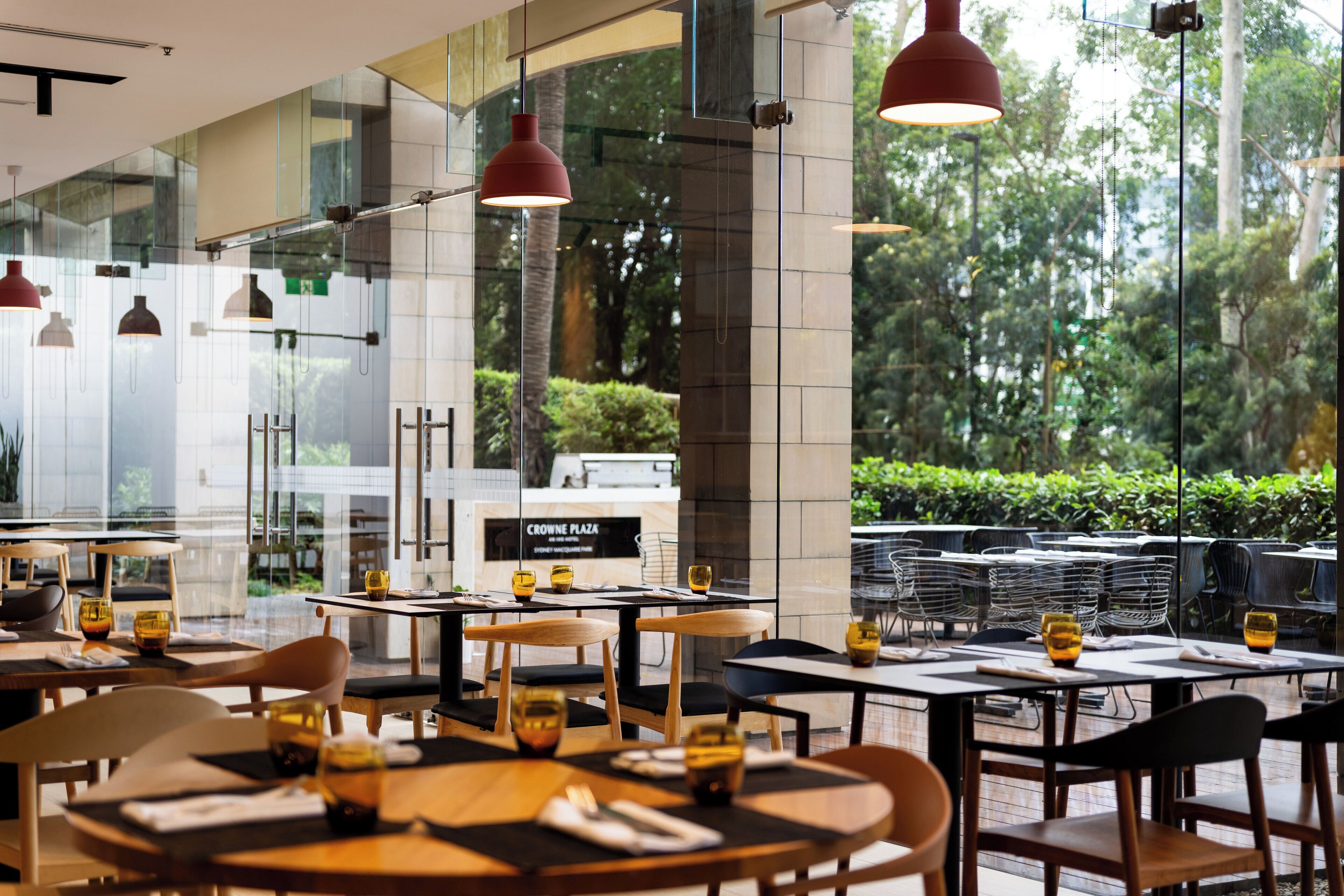 An indoor dining area with tables and chairs, large windows, and hanging pendant lights.