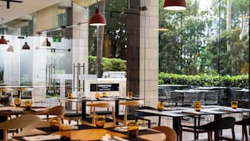 An indoor dining area with tables and chairs, large windows, and hanging pendant lights.