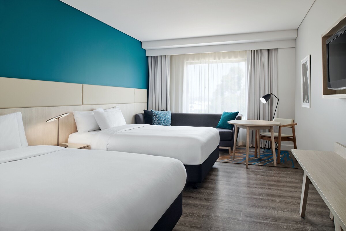 A hotel room with two beds, a sofa, a small table, and a TV.