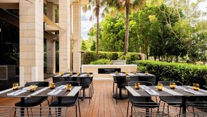 An outdoor dining area with tables and chairs, a sign reading "Crowne Plaza," and a view of trees and a building in the background. - Crowne Plaza Sydney Macquarie Park by IHG (Macquarie Park)