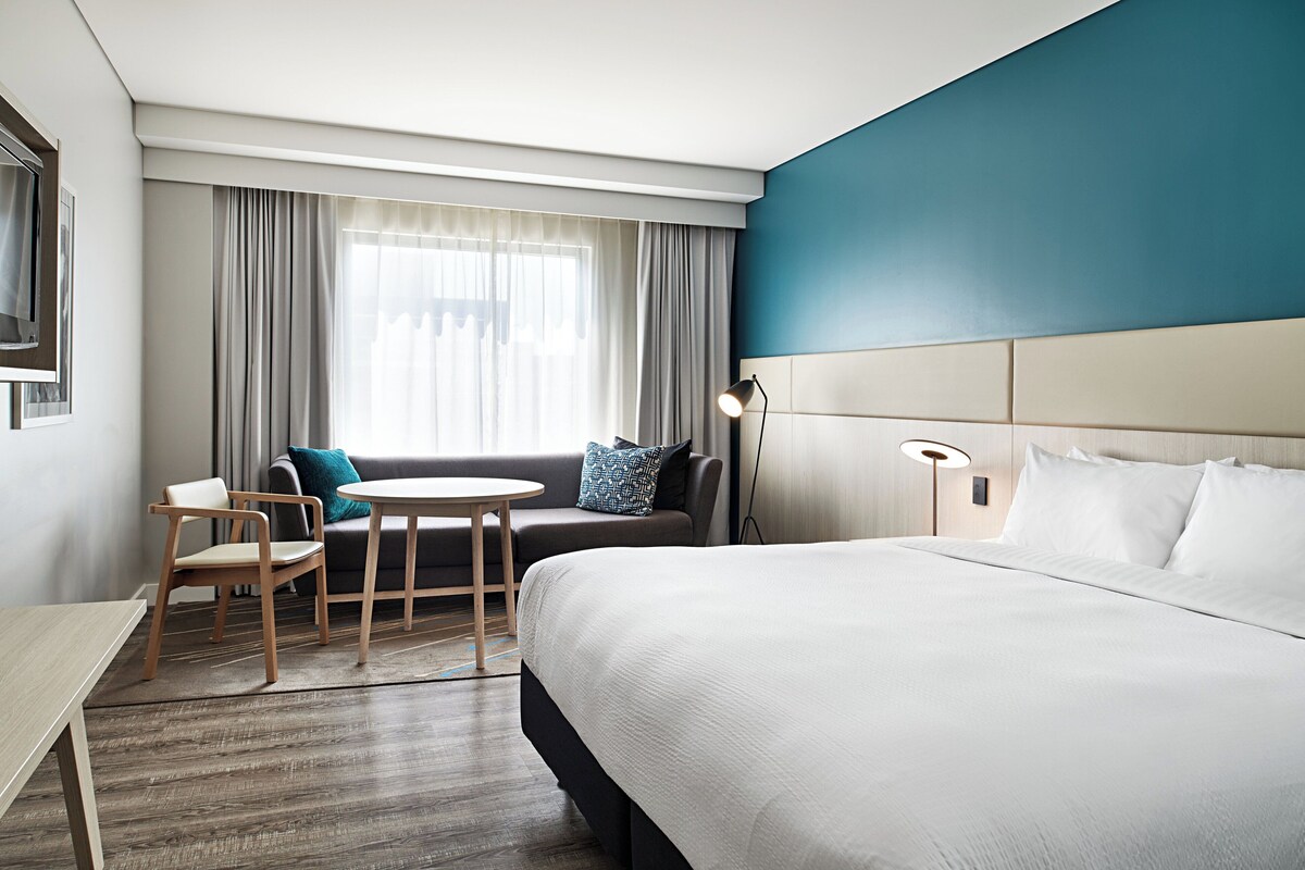 A hotel room with a large bed, a sofa, a small table, and a chair.