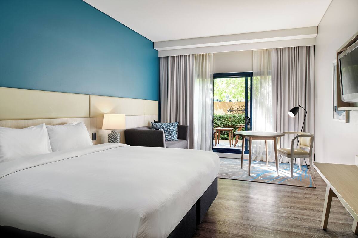 A hotel room with a large bed, a desk, a chair, a lamp, and a TV.