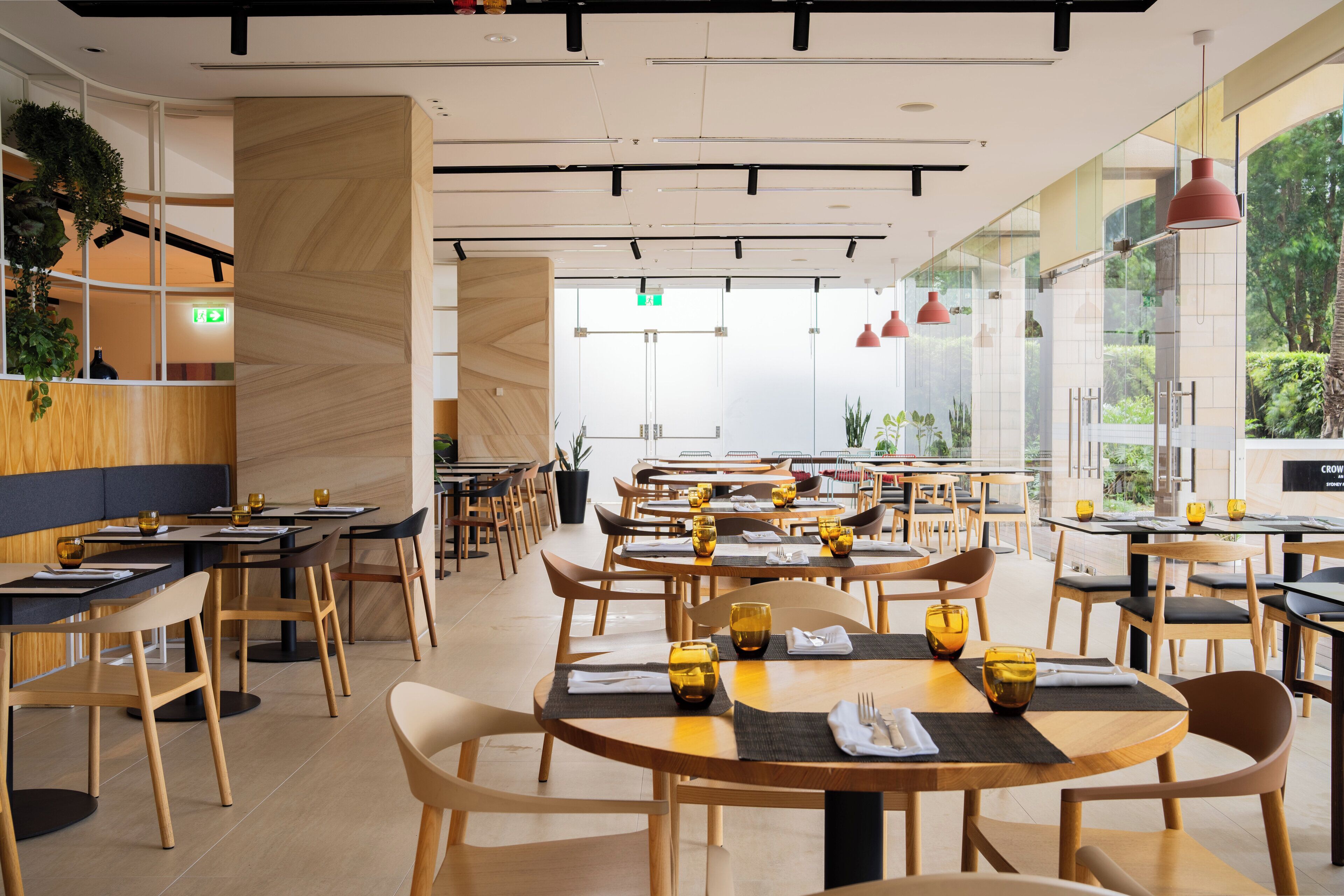 A modern restaurant with round tables, wooden chairs, and glass partitions.