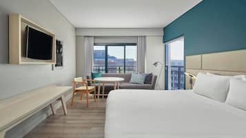 A hotel room with a large bed, a desk, a chair, a small table, a sofa, and a TV mounted on the wall.