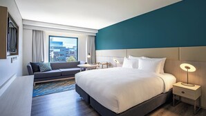 A modern hotel room with a large bed, a sofa, a small table, and a nightstand with a lamp. - Crowne Plaza Sydney Macquarie Park by IHG (Macquarie Park)