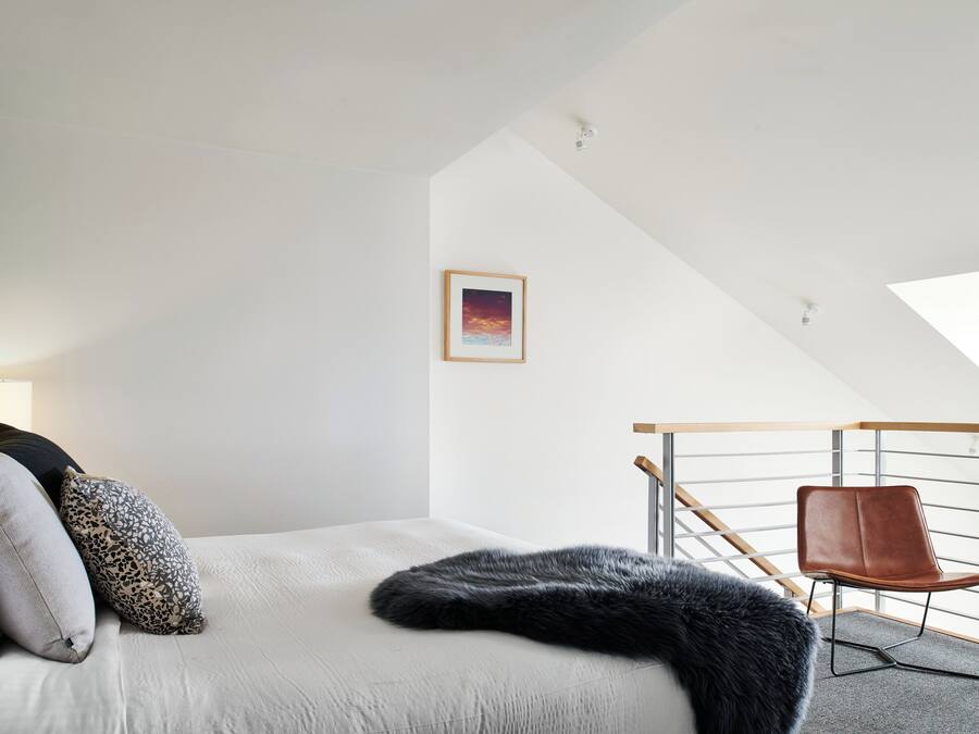 A modern bedroom with a bed, a chair, and a framed picture on the wall.