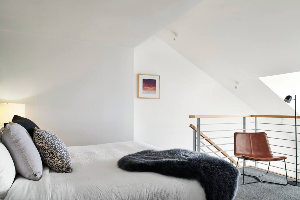 A modern bedroom with a bed, a chair, and a framed picture on the wall.