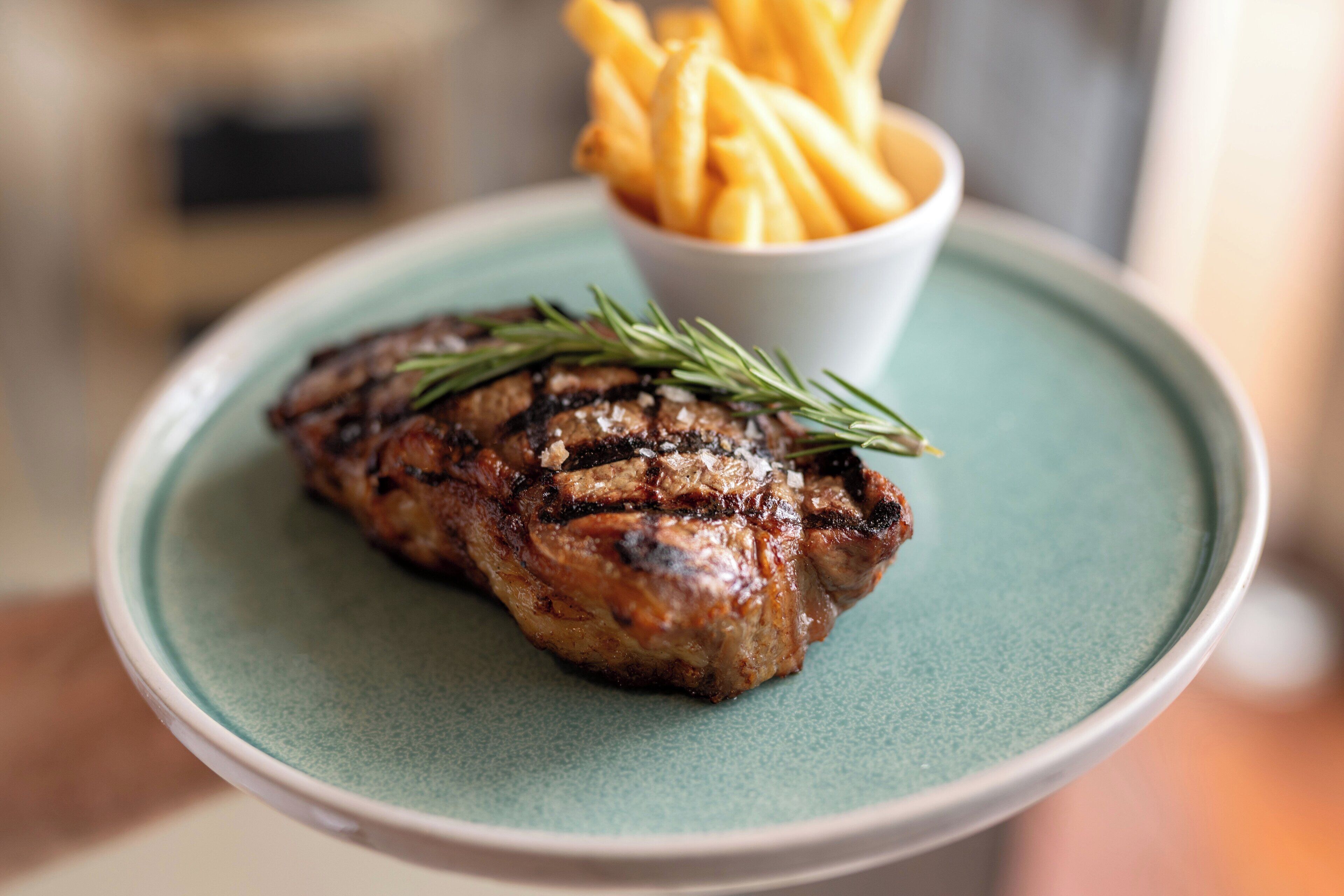 Un plato con un bistec a la parrilla y una guarnición de papas fritas.