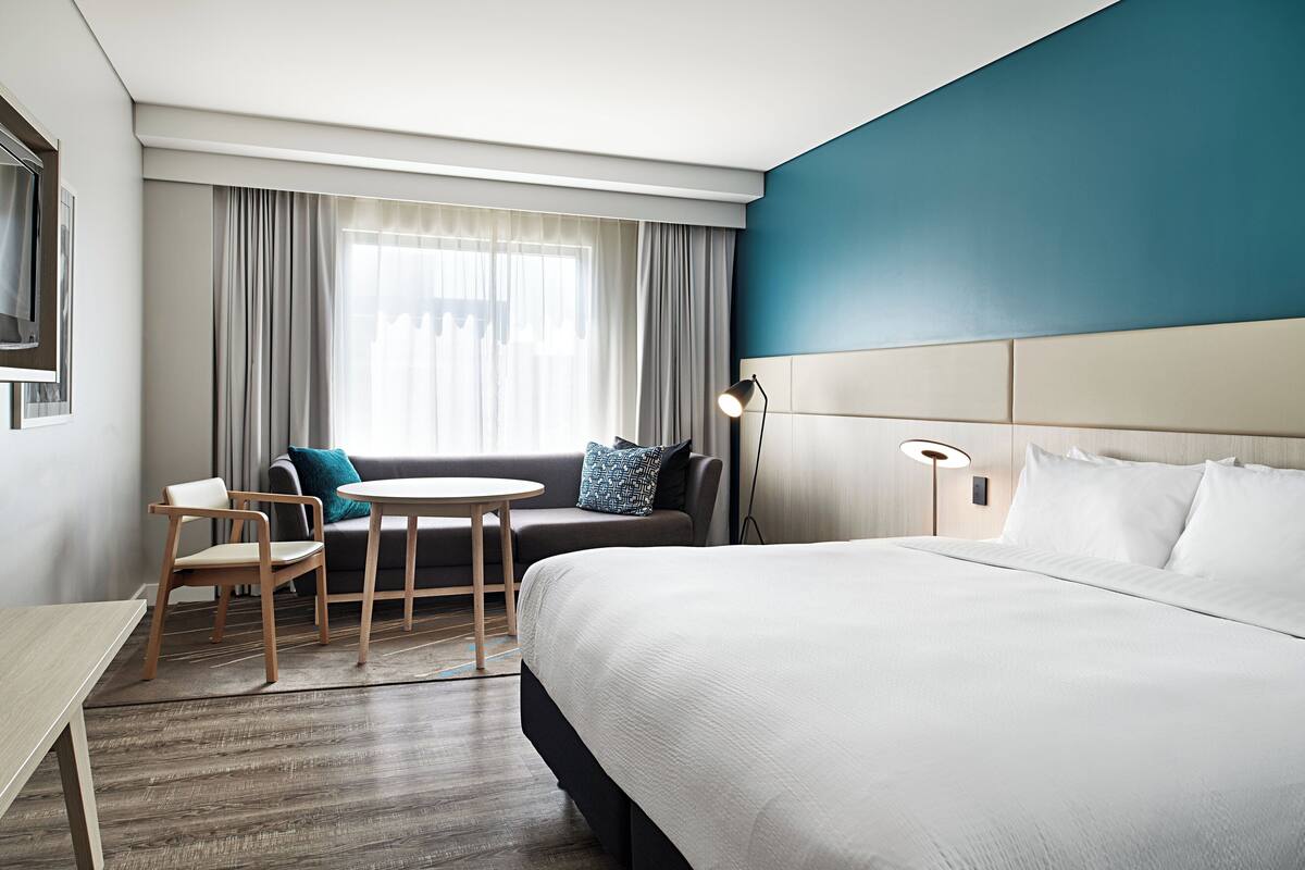 A hotel room with a large bed, a sofa, a small table, and a chair.