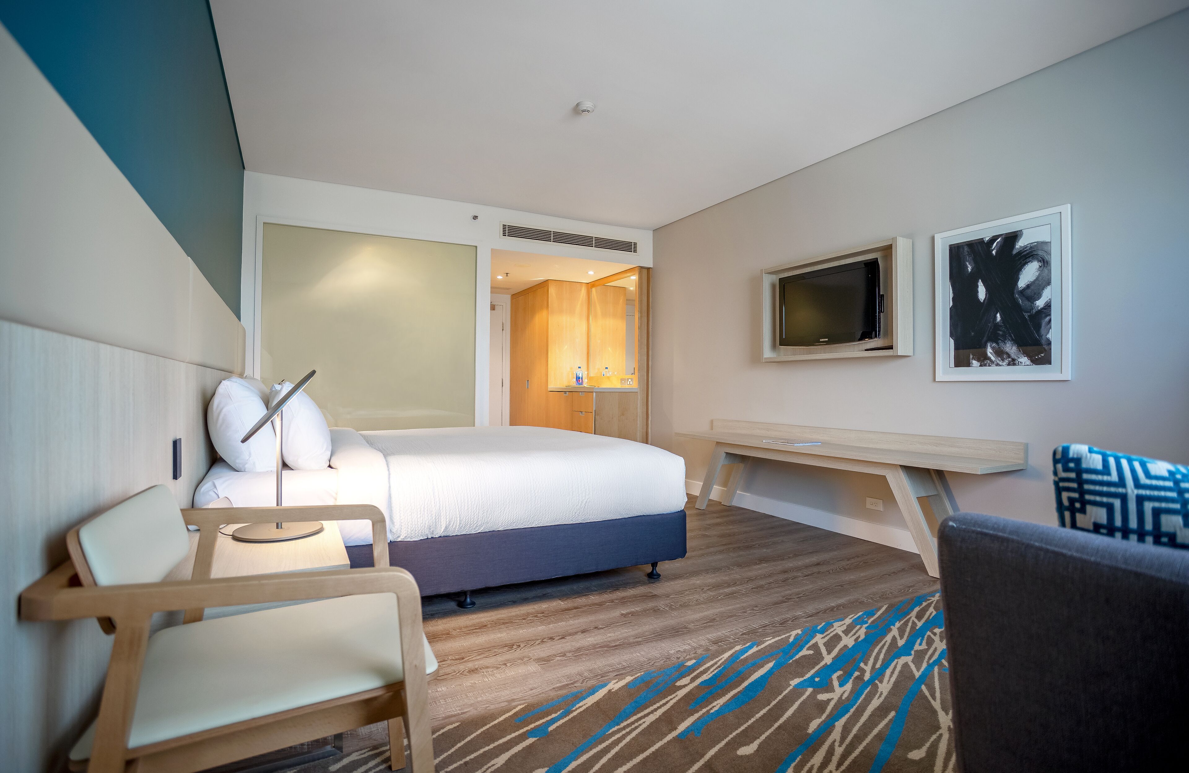Una habitación de hotel moderna con cama, mesita de noche, silla, televisor y obras de arte.