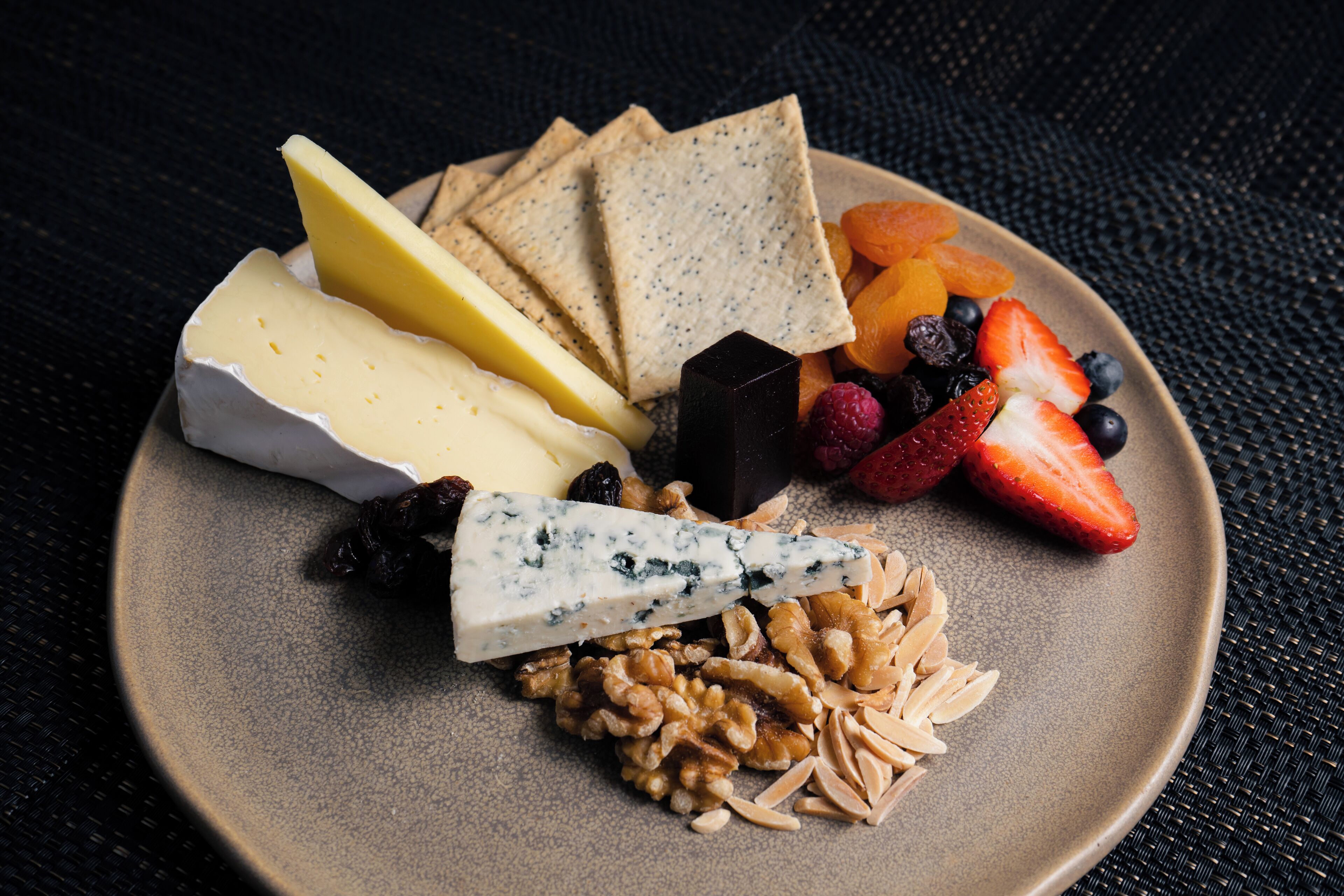 Un plato con varios quesos, galletas, frutas y frutos secos.