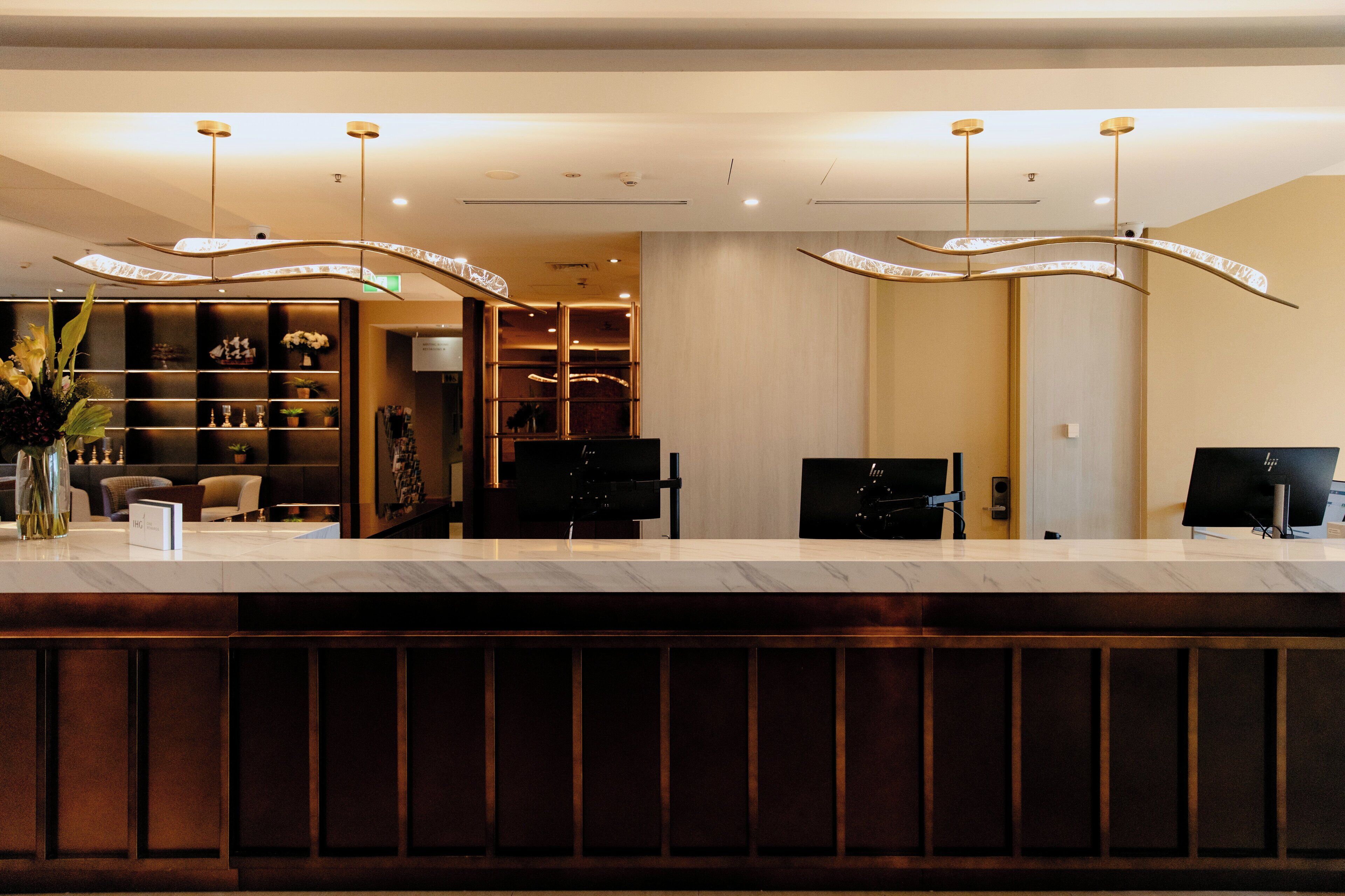 Una recepción de hotel con mostrador de mármol, luminarias modernas y un interior bien organizado.