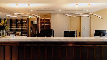 Una recepción de hotel con mostrador de mármol, luminarias modernas y un interior bien organizado.