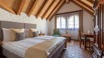 Un dormitorio con una cama grande, techo de madera, una mesita con una silla y una ventana con cortinas.