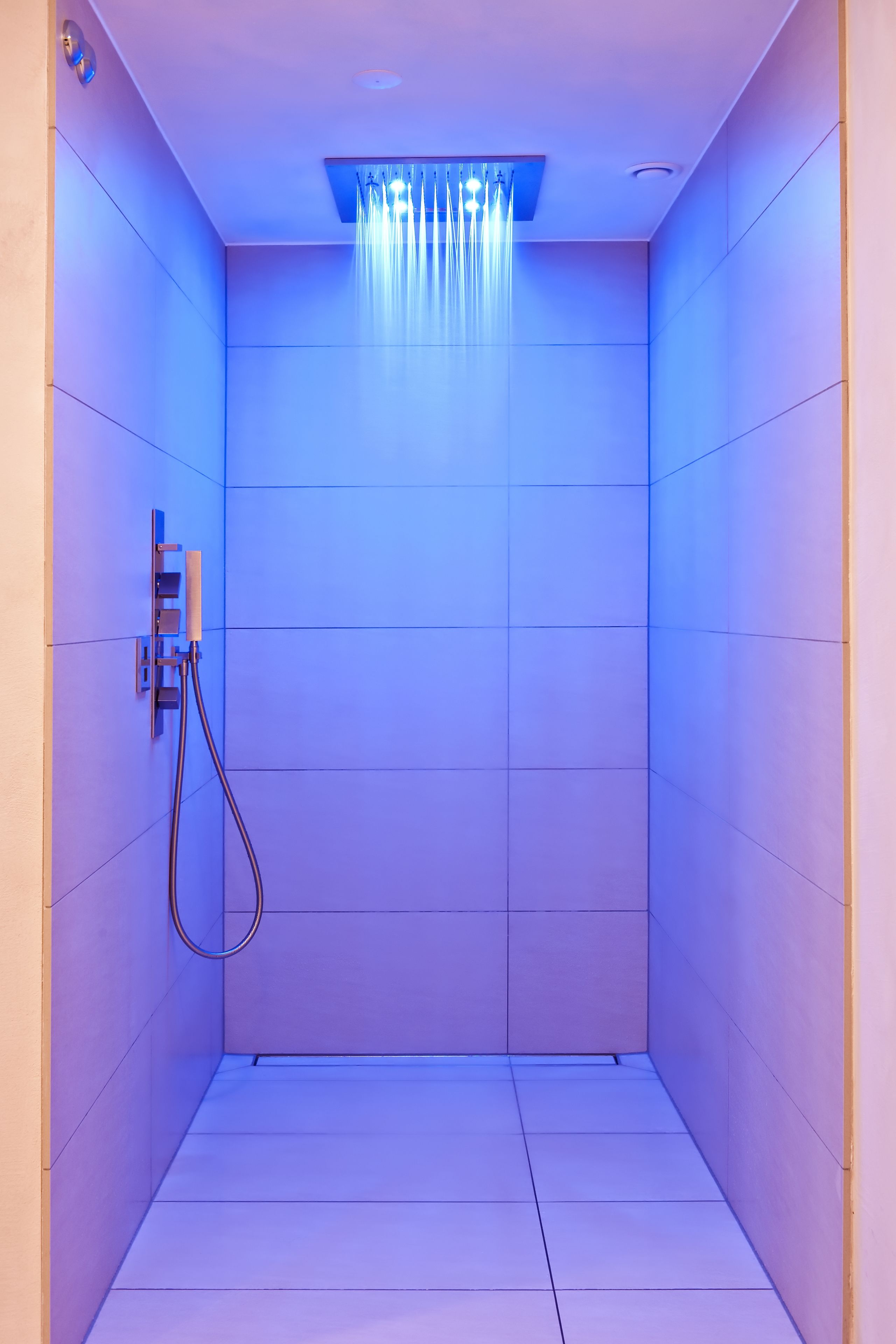 Une salle de douche moderne avec une pomme de douche illuminée en bleu et un panneau de commande fixé au mur.