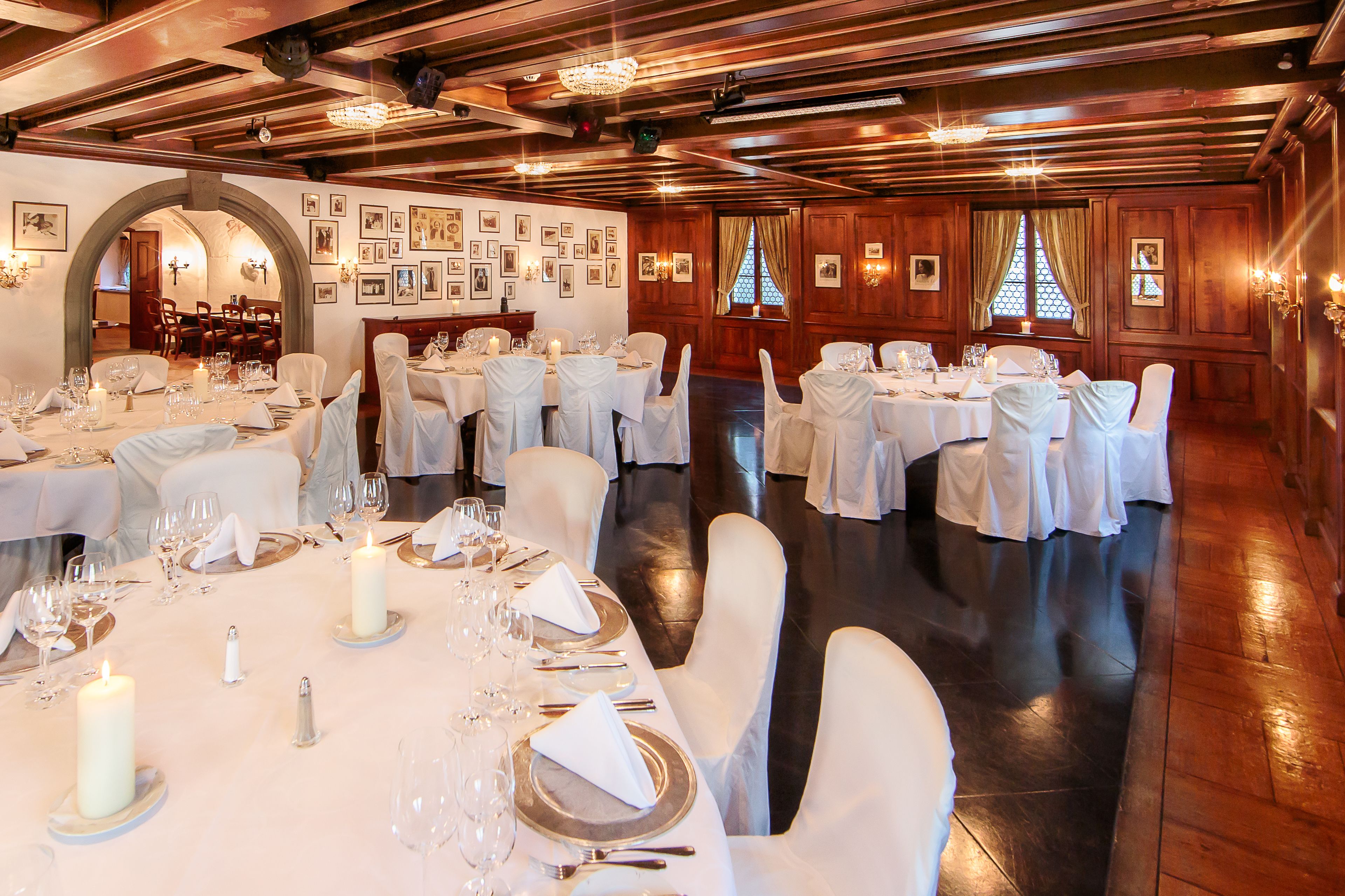 Ein formeller Speisesaal mit mehreren Tischen, die für ein Bankett gedeckt sind, mit weißen Tischdecken, Kerzen und Silberbesteck.