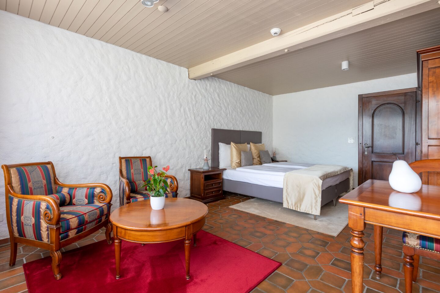A bedroom with a bed, two chairs, a small table, and a nightstand.