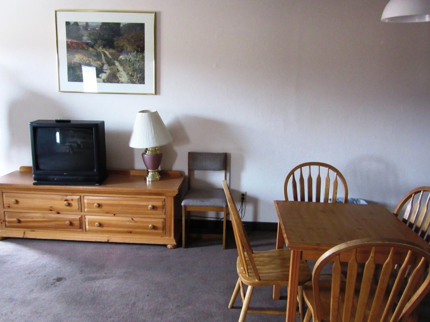 Una habitación con un aparador de madera, televisor, lámpara, un cuadro en la pared y una mesa de comedor de madera con sillas.