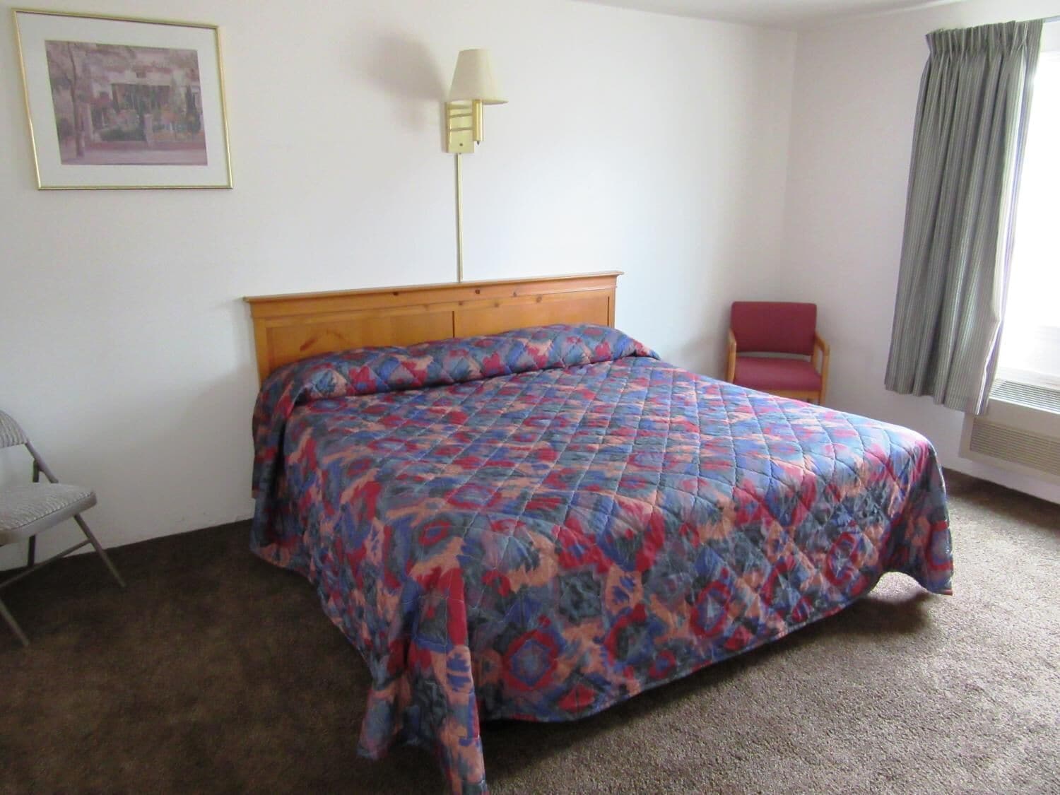 A bedroom with a bed, a chair, a lamp, and a window with curtains.