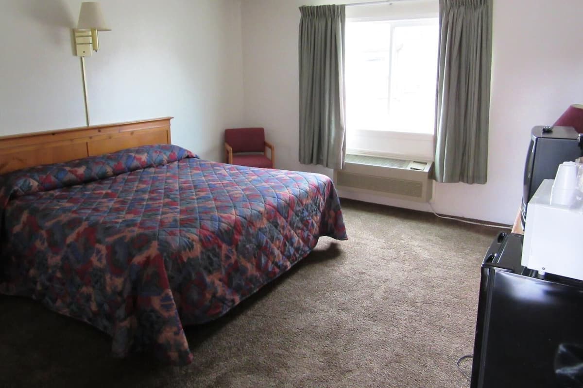 A hotel room with a bed, a chair, a desk, and a window with curtains.