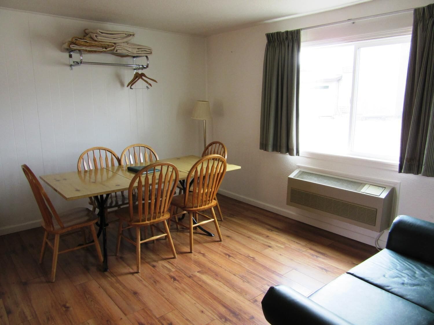A dining area with a wooden table and chairs, a lamp, a window with curtains, and a radiator.