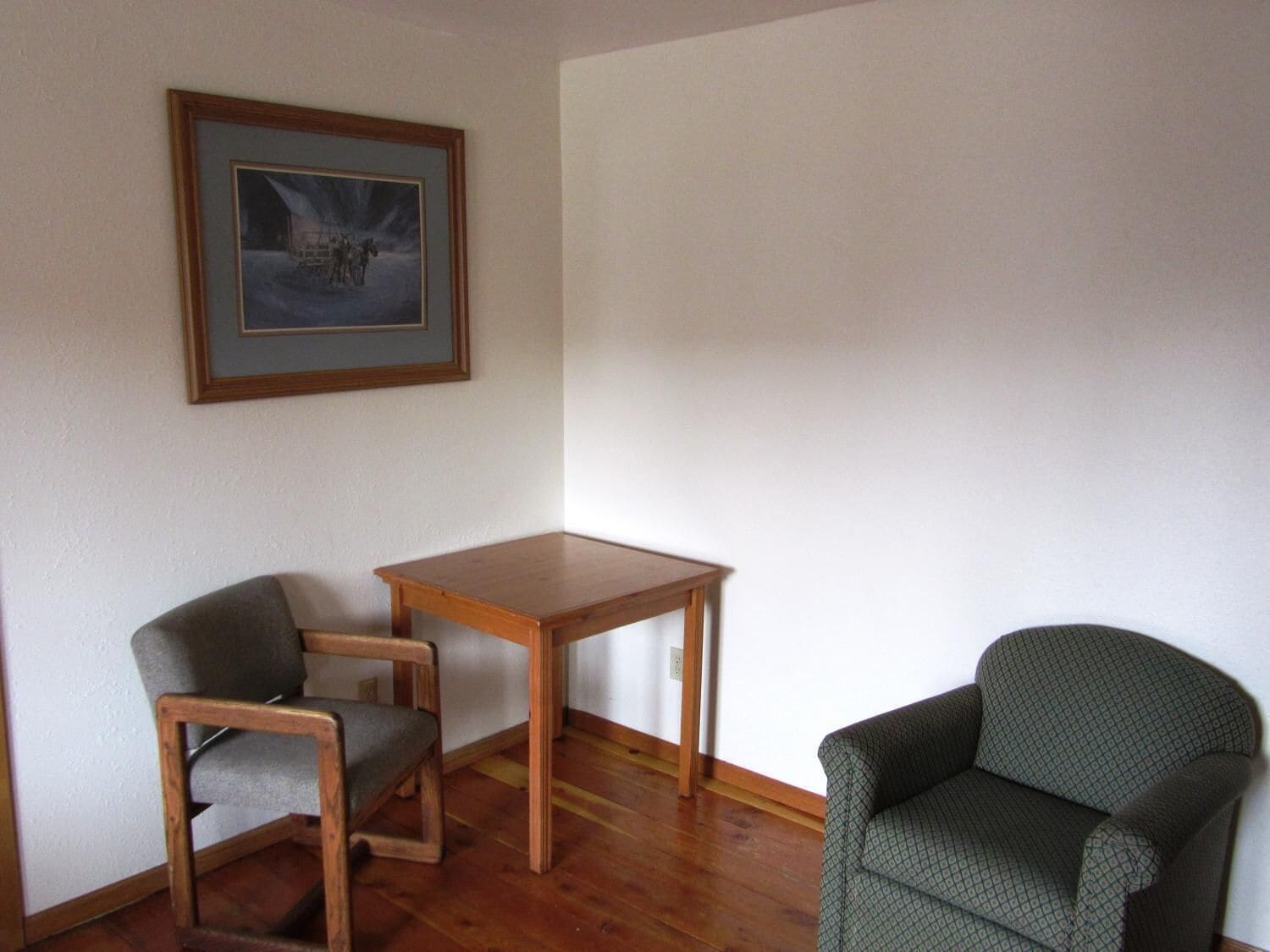Une pièce avec une table en bois, deux chaises et un tableau encadré accroché au mur.